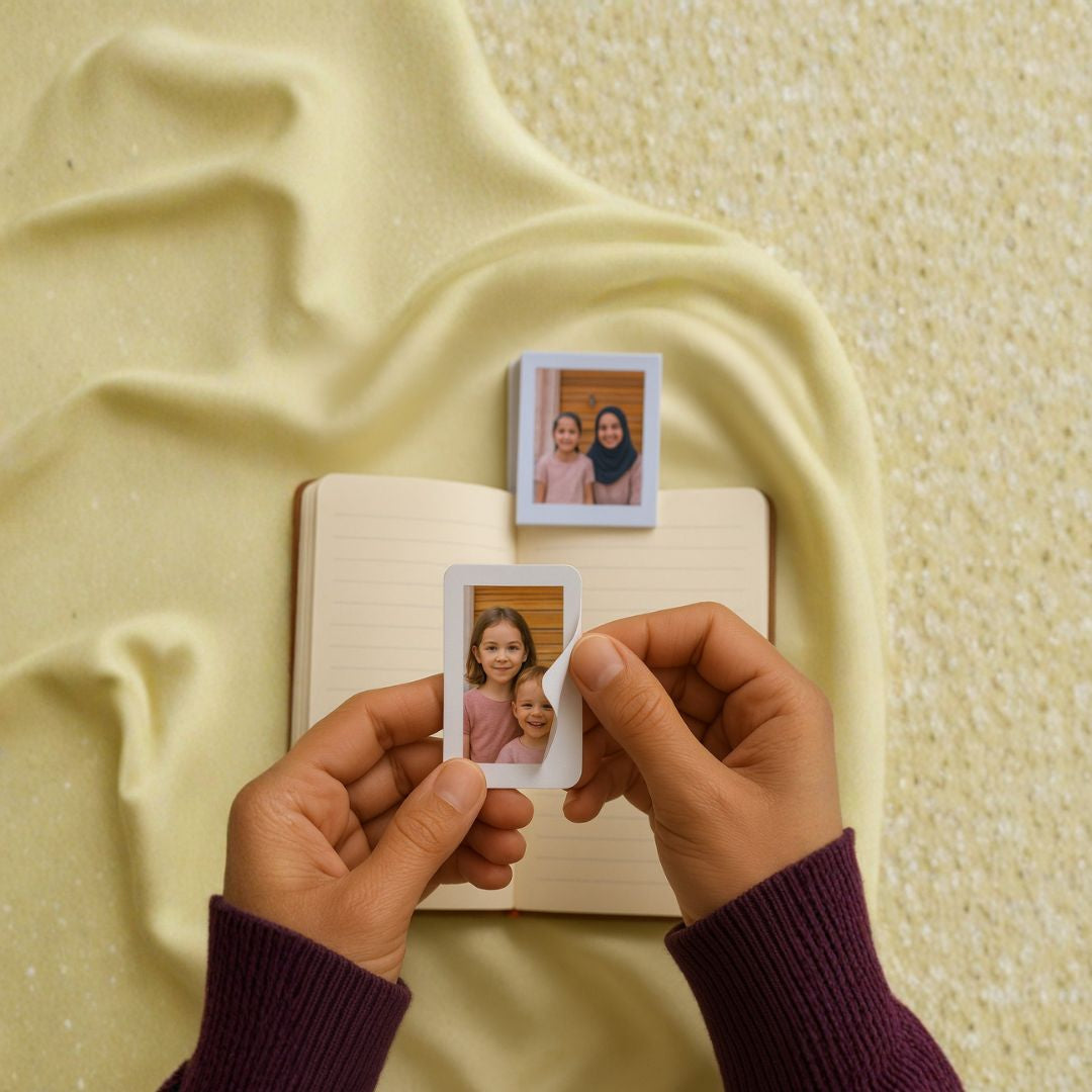 Two small polaroid photo prints of a young girl held by hands & being peeled to stick in a diary