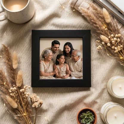 Family photo in a black color photo frame surrounded by dried plants and candles on a textured surface