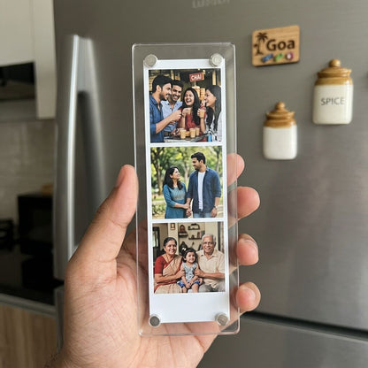 Hand holding a transparent acrylic fridge magnet strip with family photos in front of a refrigerator.