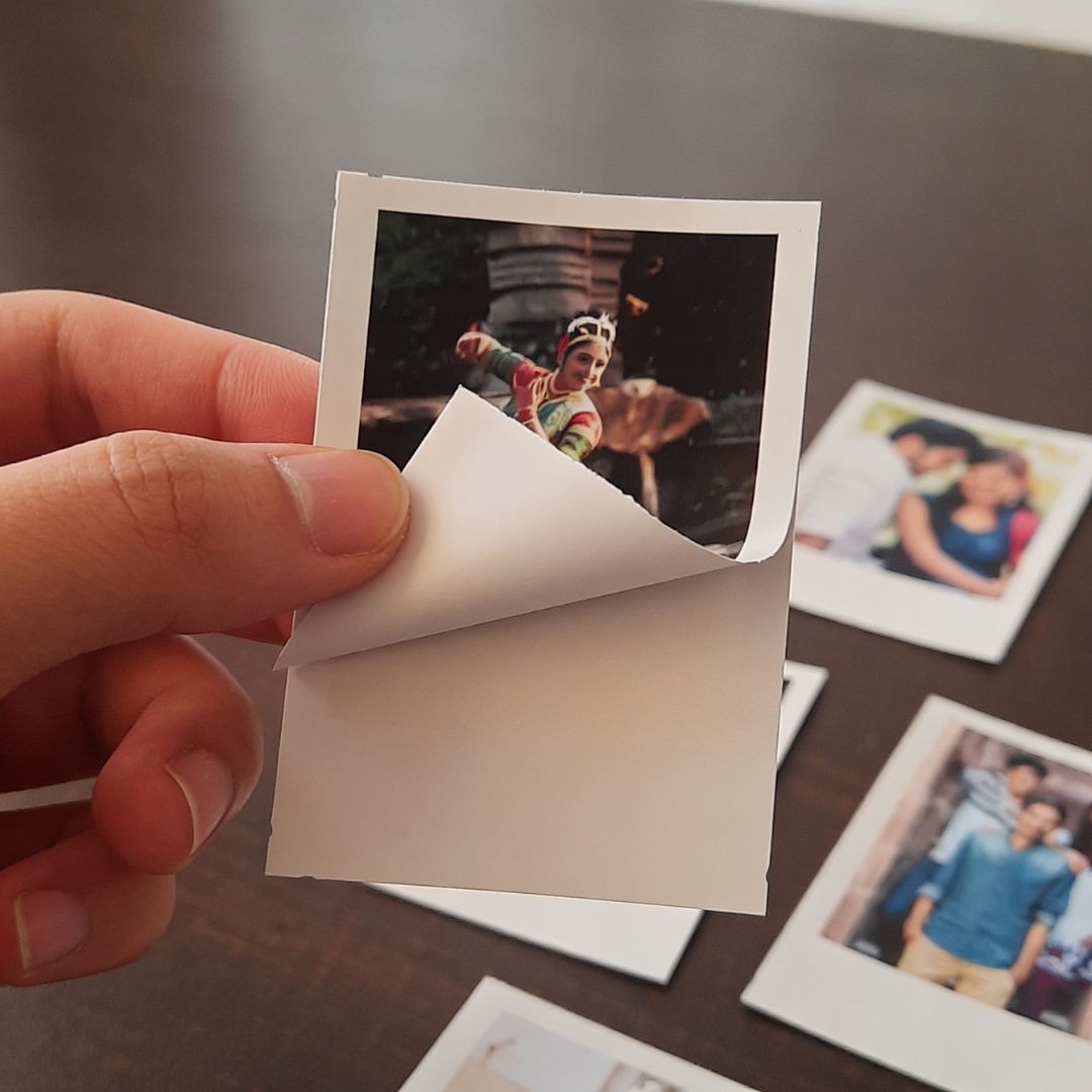 Hand holding a peel and stick kind of small Polaroid photo print with more adhesive polaroid photos in the background