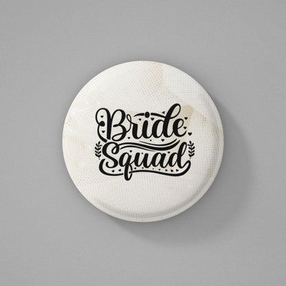 Round shaped pin badge with 'Bride Squad' text written on it and placed on a gray background