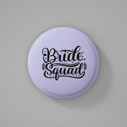Round purple pin badge with 'Bride Squad' text written on it and kept on a gray background