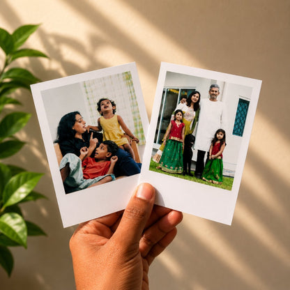 Two Polaroid photos held by a hand against a beige wall with plant shadows.