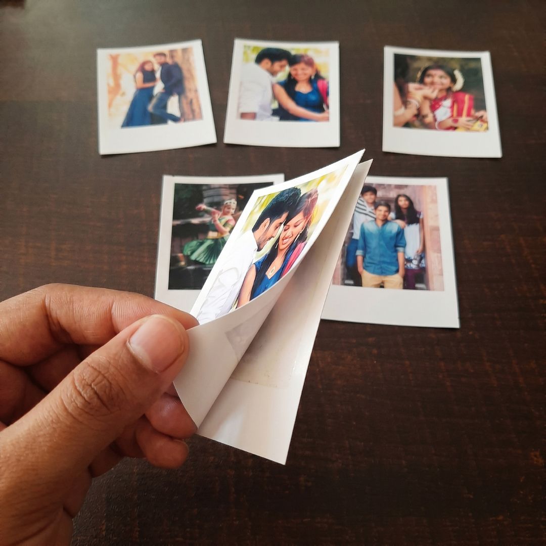 Hand holding a photo of a couple printed on a peel and stick paper  with other Polaroid-style photos