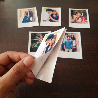 Hand holding a photo of a couple printed on a peel and stick paper  with other Polaroid-style photos